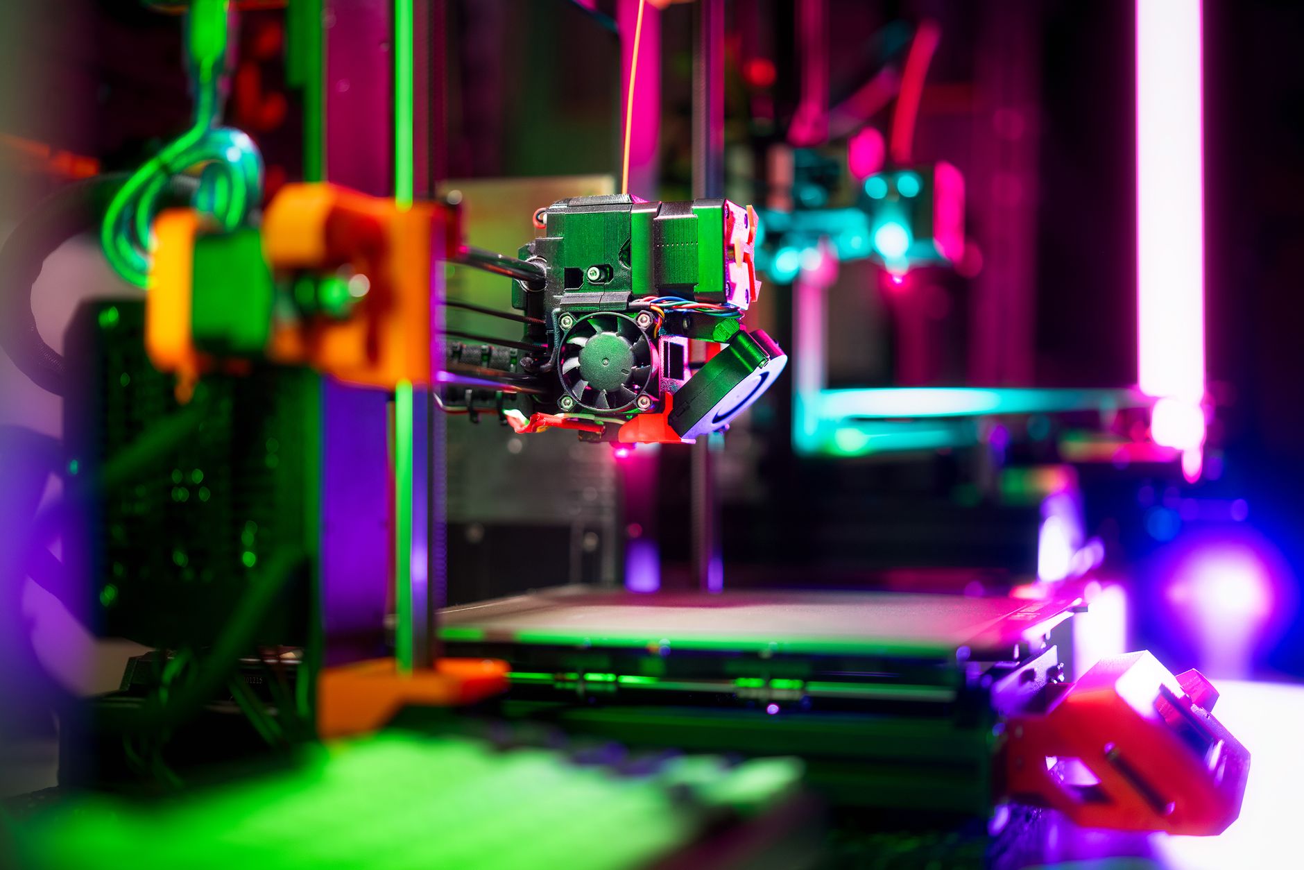 A 3D printer extruder feeds orange filament while printing small parts on its build plate.